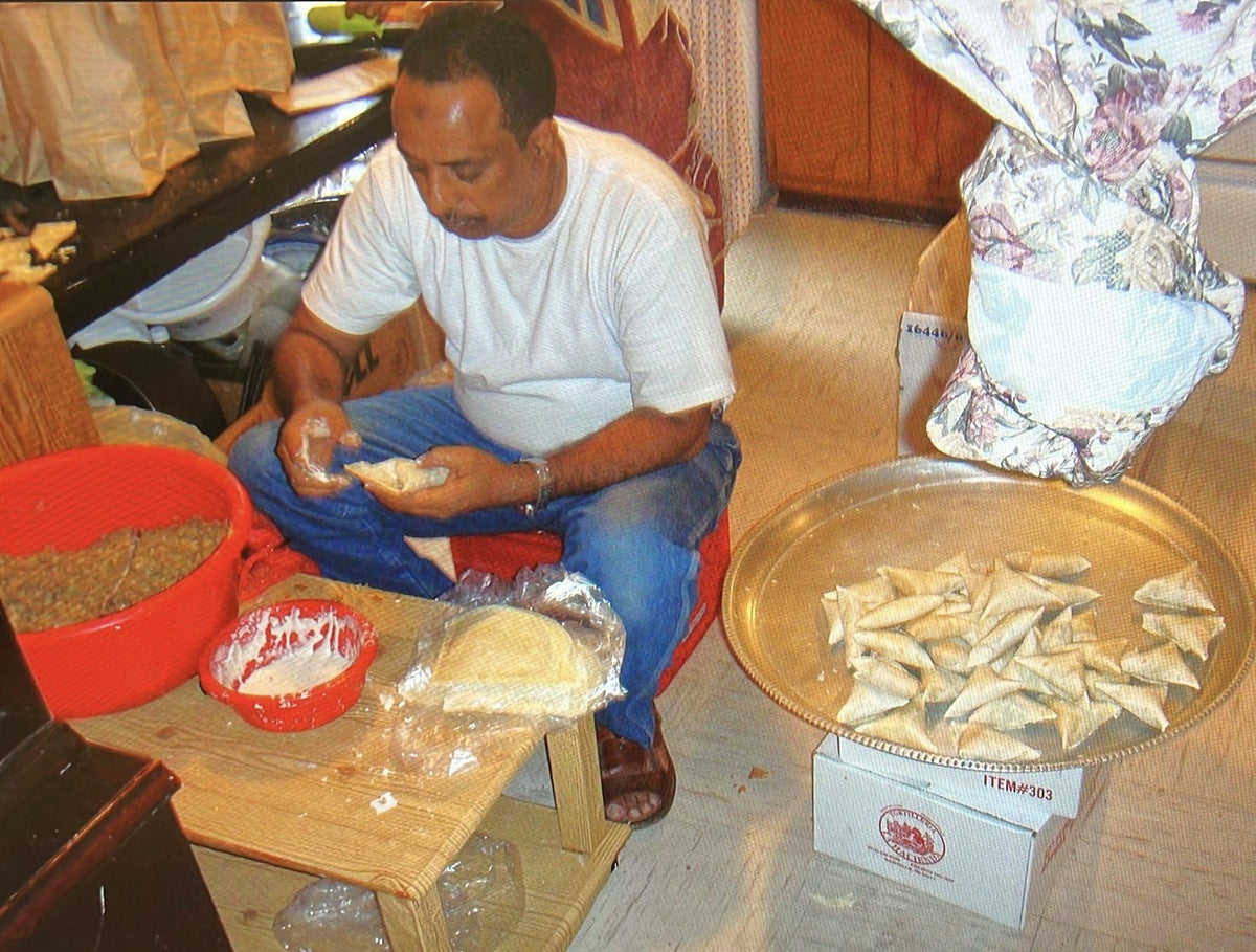 Dad folding sambusas by hand next to a tray of folded sambusas