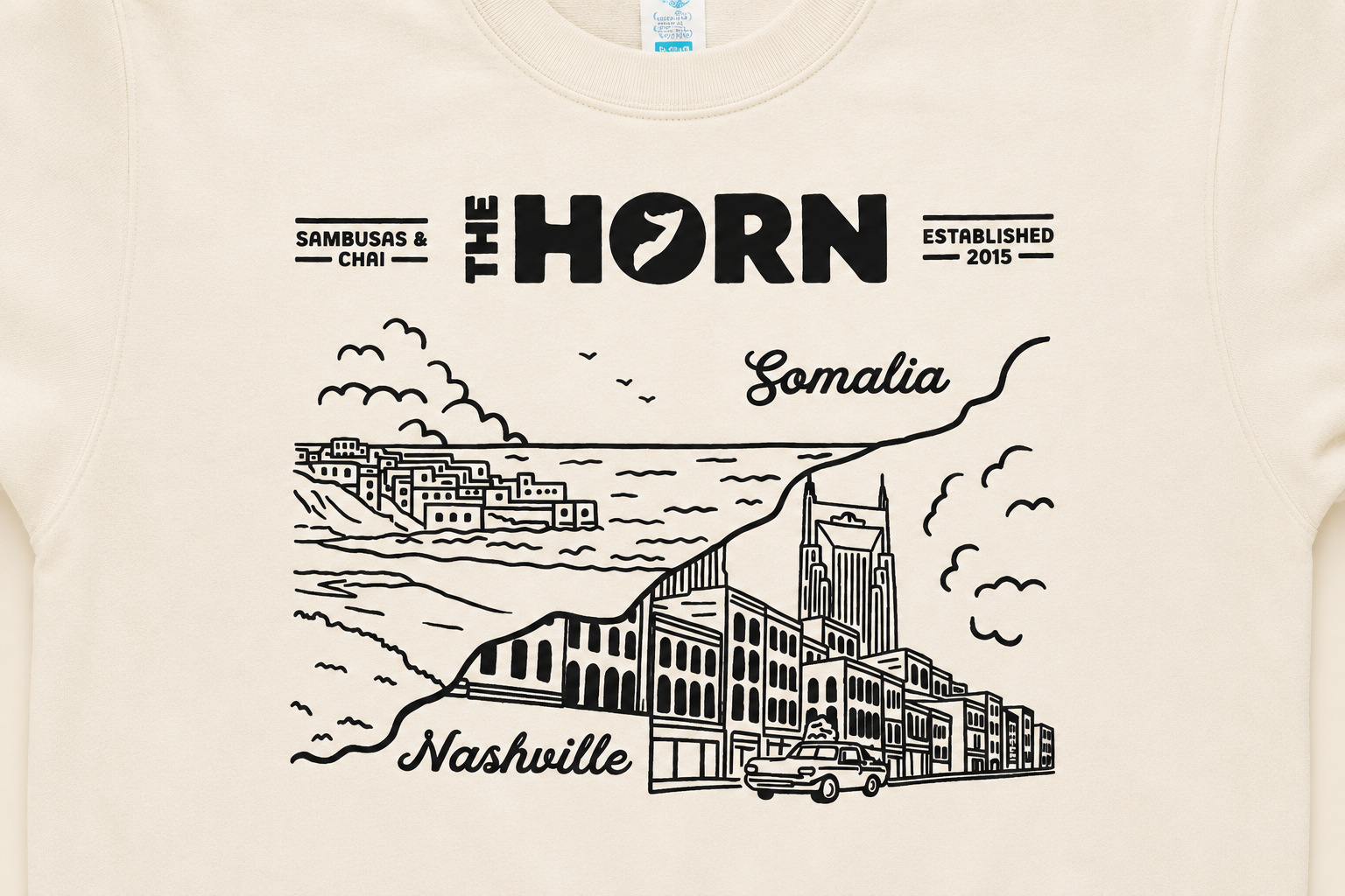 Beige t-shirt with black graphic design featuring 'The Horn' restaurant branding and a cityscape illustration.