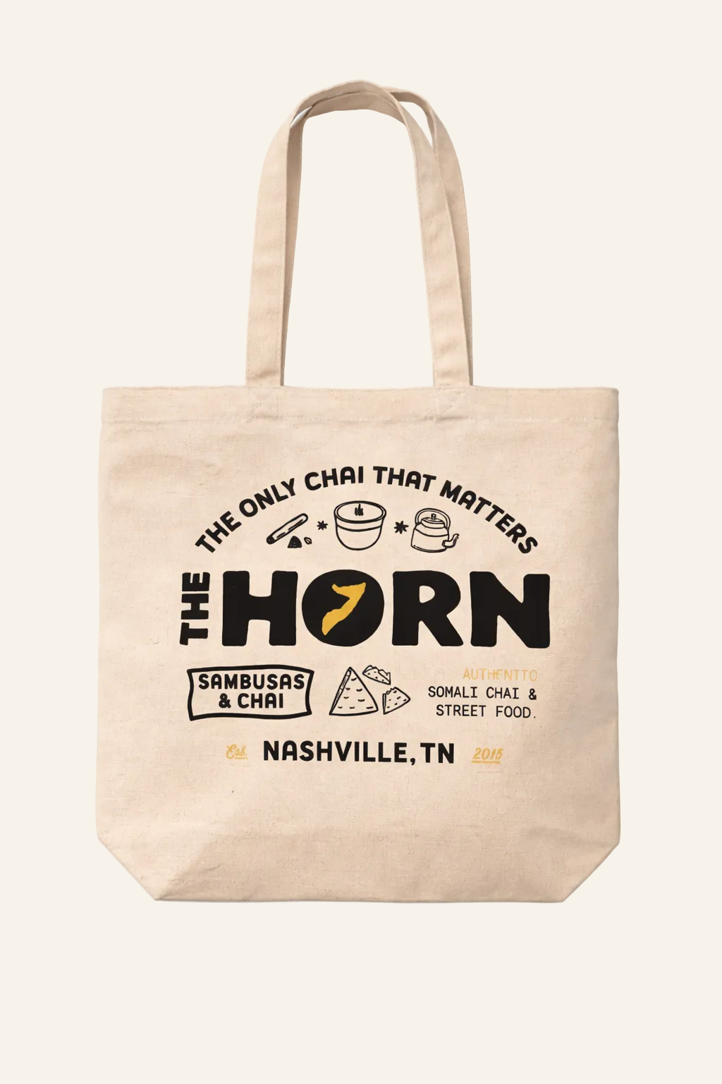 Beige tote bag with 'The Horn' branding and text on a white background