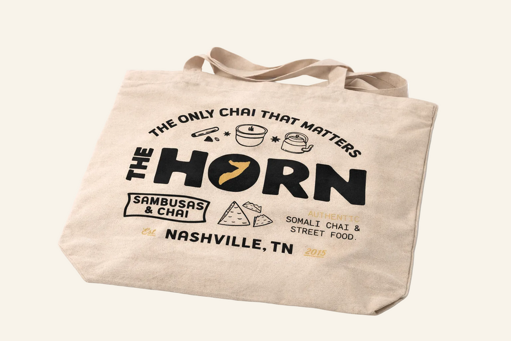 Beige tote bag with 'The Horn' branding and text on a white background