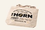 Beige tote bag with 'The Horn' branding and text on a white background