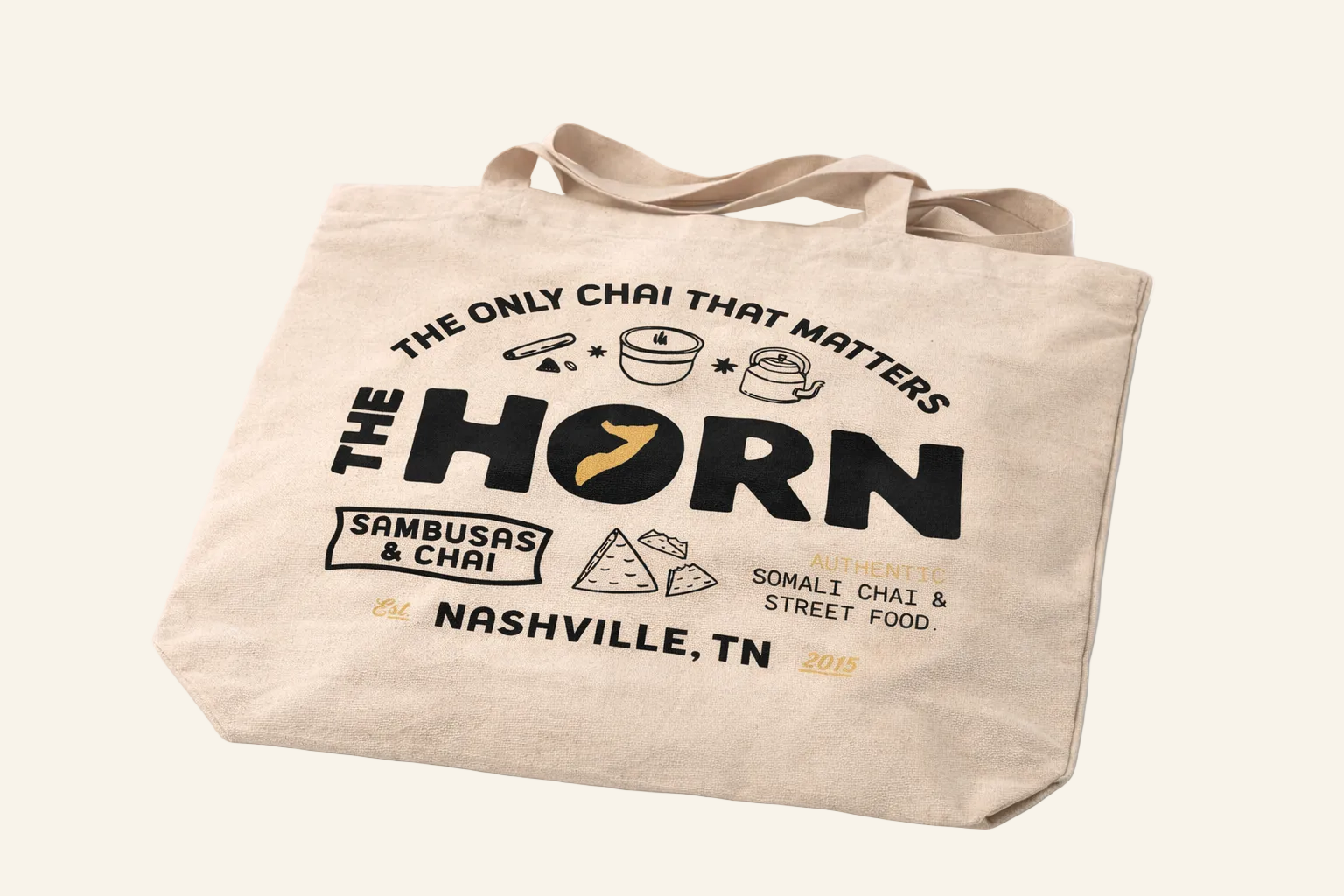 Beige tote bag with 'The Horn' branding and text on a white background