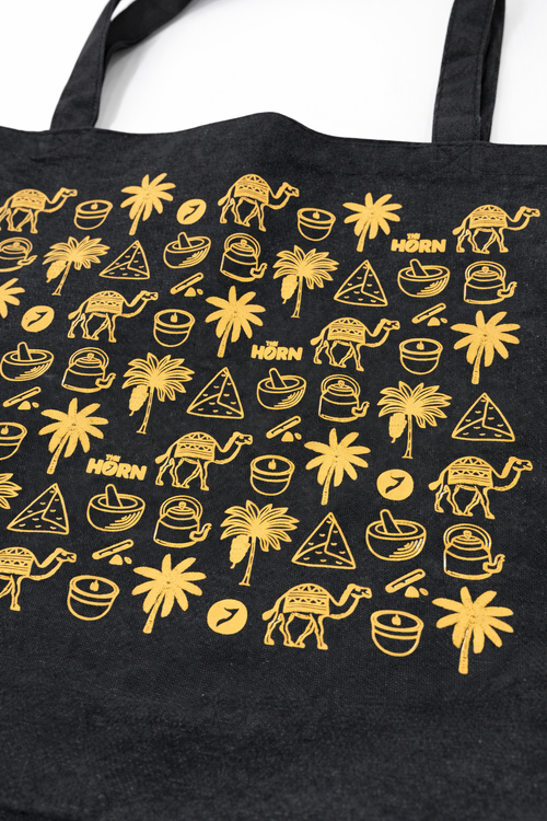 Black tote bag with gold illustrations of palm trees, camels, and other desert-themed designs.
